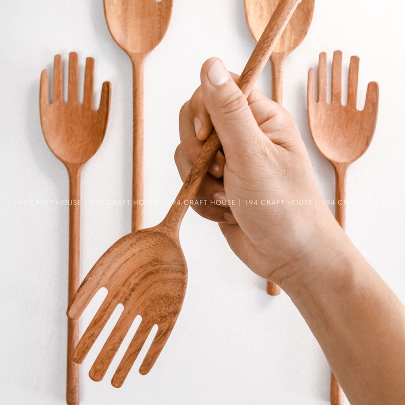 May include: A set of five wooden kitchen utensils with a hand-shaped design. The utensils are made of natural wood and have a warm brown color.