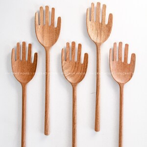 May include: Set of five wooden hand-shaped serving spoons. The spoons have a long handle and a hand-shaped head with five fingers.