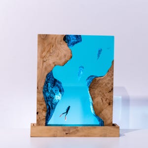 Könnte beinhalten: Ein hölzernes Kunstwerk mit einer blauen Harz-Ozeanszene, Quallen und einem Taucher. Der Rahmen hat eine natürliche Holzmaserung. Das Kunstwerk steht auf einem Holzsockel.