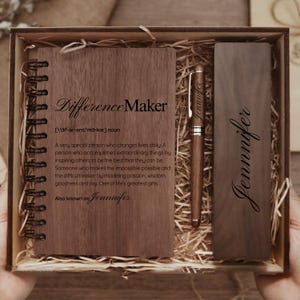 May include: A wooden gift set containing a notebook, pen, and bookmark. The notebook is inscribed with "Difference Maker" and a definition. The pen and bookmark are engraved with the name "Jennifer". The set is presented in a wooden box.