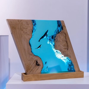 Könnte beinhalten: Ein Holzkunstwerk mit einer blauen Flusslandschaft aus Kunstharz, die Wale und Taucher zeigt. Das Kunstwerk ist in einem Holzrahmen und Sockel gefasst und schafft eine einzigartige, beleuchtete Darstellung. Das Stück ist abgewinkelt und zeigt die Tiefe der Meereslandschaft.