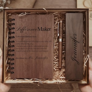 May include: A wooden gift set comprising a notebook, pen, and bookmark, all with a dark wood finish. The notebook reads "Difference Maker" with a definition. The pen and bookmark are engraved with the name "Jennifer". The set is presented in a wooden box.