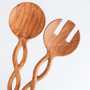 May include: A set of two wooden salad servers with a twisted handle design. The server on the left is a spoon and the server on the right has two prongs.