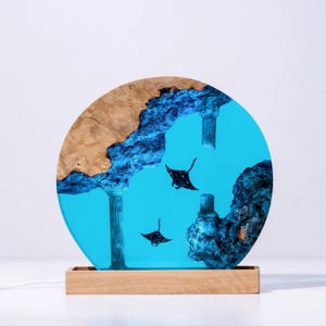 Könnte beinhalten: Runde, dekorative Lampe mit einer blauen Harz-Ozeanszene mit Mantarochen. Die Lampe hat einen Holzsockel und einen oberen Teil mit Holzmaserung und blauem Harz. Die Lampe enthält ein Netzkabel.
