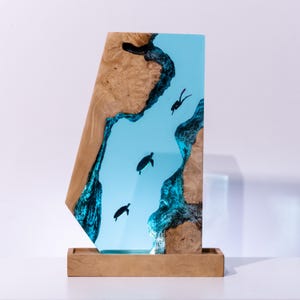 Könnte beinhalten: Ein Holz- und Kunstharz-Kunstwerk mit einer hellblauen Flussszene mit Tauchern und Schildkröten. Der Holzrahmen hat eine natürliche Maserung, und das Kunstharz erzeugt einen durchscheinenden Effekt. Auf einem Holzsockel montiert.