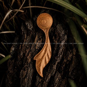 May include: A small, hand-carved wooden spoon with a circular bowl and a handle shaped like a leaf. The wood features a rich, warm brown tone with visible natural grain patterns. The text 194 CRAFT HOUSE is repeated across the image.