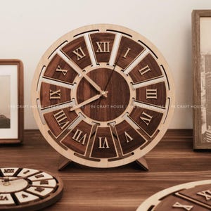 May include: A wooden clock with a light-colored frame and dark brown interior. The clock face features Roman numerals and hands. The clock is displayed on a wooden surface.