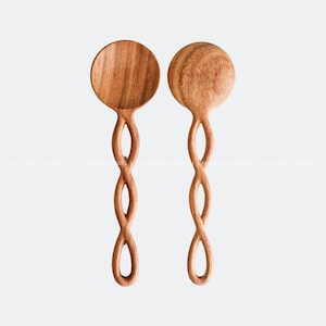 Op de afbeelding: Twee houten lepels met gedraaide handvatten. De lepels zijn gemaakt van lichtbruin hout en hebben een ronde komvorm.