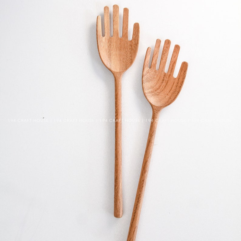 May include: Two wooden hand-shaped salad servers. The servers are made of light brown wood and have a natural finish.