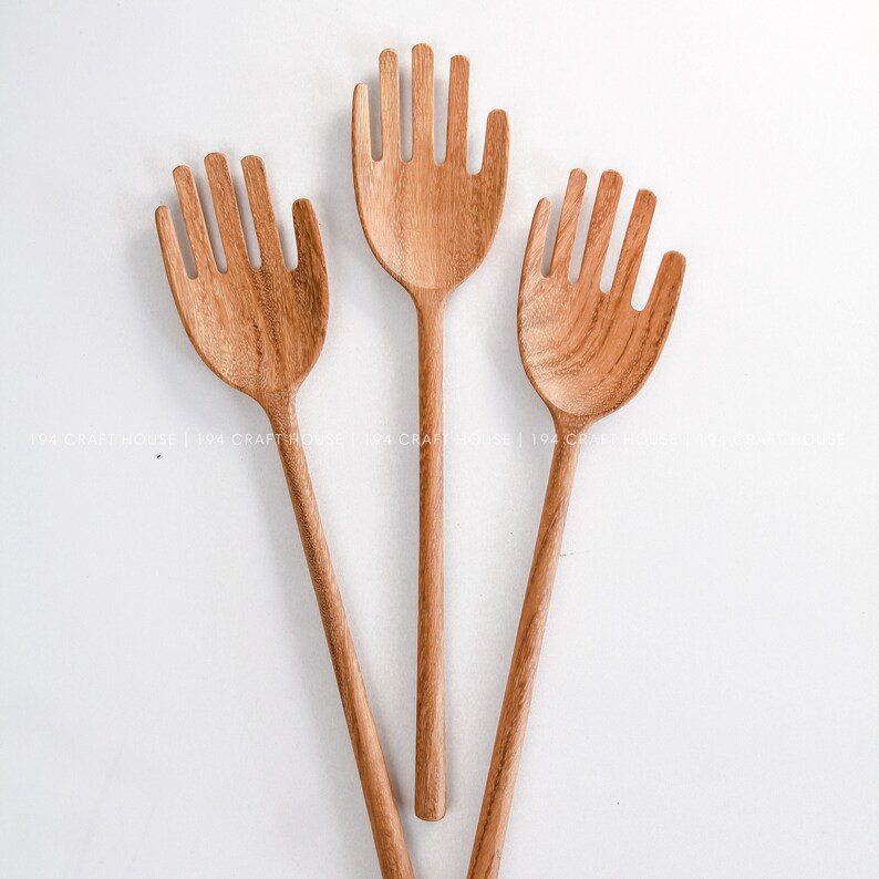 May include: Three wooden hand-shaped kitchen utensils with holes in the spoon part. The utensils are brown and have a natural wood finish.