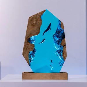 Könnte beinhalten: Ein dekoratives Holzkunstwerk mit einer lebendigen blauen Harz-Ozeanszene mit Walen und Tauchern. Das Kunstwerk ist in einem Holzrahmen eingefasst und steht auf einem Holzsockel, wodurch ein einzigartiges Display entsteht.
