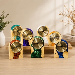 May include: Six arched desk clocks featuring natural wood bases with embedded colorful resin accents in teal, purple, white, orange, green, and blue. Each clock has a circular gold face with black Roman numerals and black hands.