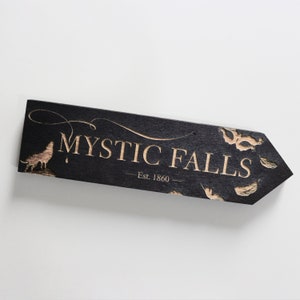 May include: Black wooden sign with the text "Mystic Falls - Est. 1860" in gold lettering. The sign is shaped like an arrow pointing to the right.