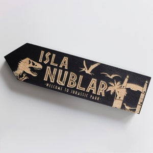 May include: Black wooden sign with the words "Isla Nublar - Welcome to Jurassic Park" in a vintage style font. The sign also features a dinosaur, a pterosaur, and a palm tree.