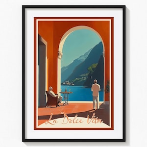 May include: Framed art print of a vintage travel poster. The image shows an Italian lakeside scene with mountains, an archway, and the text "La Dolce Vita". Two figures are present, one seated and one standing, enjoying the view.