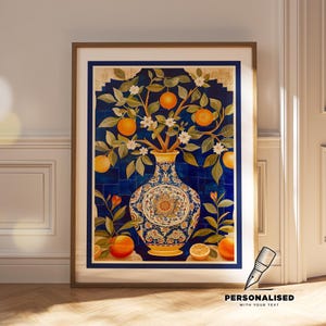 Op de afbeelding: Ingelijste kunstdruk met een illustratie van een sinaasappelboom in een decoratieve vaas. Het kunstwerk toont een blauwe achtergrond met een gedetailleerd vaasontwerp, sinaasappels en witte bloesems. De lijst is bruin.