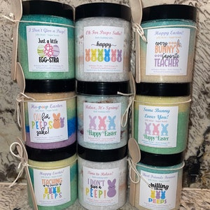 May include: Nine jars of bath salts with colorful sugar scrubs. Each jar has a different Easter-themed design with a peep and a funny saying. The jars are arranged in three rows of three.