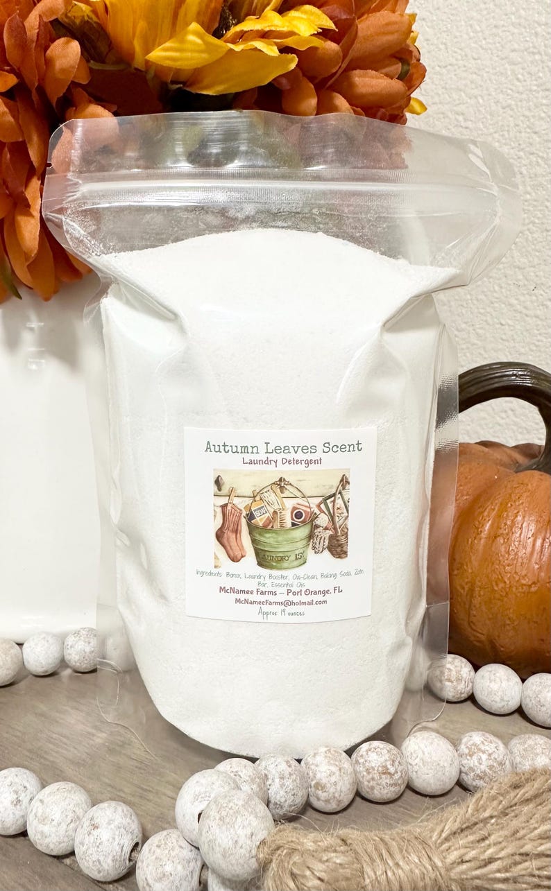 Op de afbeelding: Een witte hersluitbare zak gevuld met wasmiddelpoeder. Het etiket luidt "Autumn Leaves Scent Laundry Detergent" met een tekening van een wasmand en een paar sokken. Het etiket bevat ook de ingredi&euml;nten, de bedrijfsnaam "McNamee Farms", de locatie "Port Orange, FL", het e-mailadres "McNameeFarms@hotmail.com" en de grootte "Approx 19 ounces".