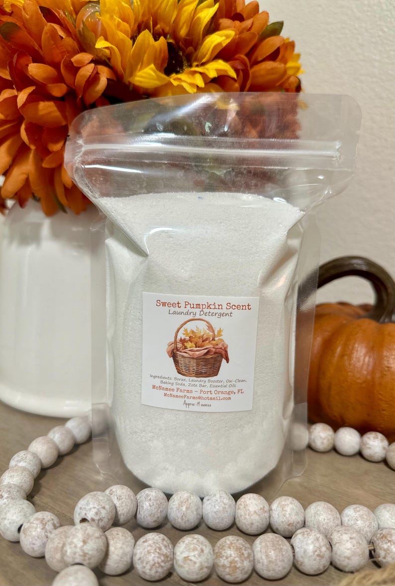 Op de afbeelding: Een witte hersluitbare plastic zak gevuld met wit wasmiddelpoeder. De zak heeft een label met de tekst "Sweet Pumpkin Scent Laundry Detergent" met een mand vol herfstbladeren en de tekst "Melance Farms - Port Orange, FL MelanceFaras@hotmail.com".