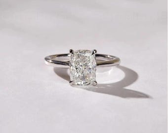 May include: A silver engagement ring with a large, rectangular-cut diamond. The diamond is the focal point, set on a thin, polished band. The ring is displayed on a white surface, casting a shadow.
