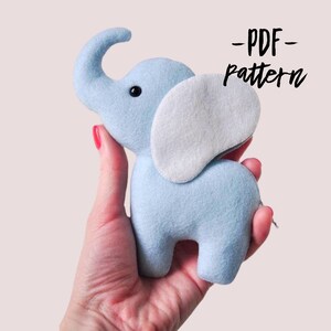 Könnte beinhalten: Ein hellblaues Filz-Elefanten-Plüschtier mit einem weißen Filzohr. Das Spielzeug wird in der Hand einer Person gehalten. Der Text -PDF- pattern ist in Schwarz auf weißem Hintergrund geschrieben.