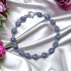 May include: A silver wire wrapped necklace with grey and purple glass beads.