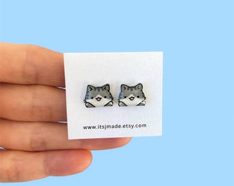 May include: A pair of stud earrings shaped like cartoon gray and white tabby cats with small pink noses and open mouths. The earrings are attached to a white display card featuring the text www.itsjmade.etsy.com printed in black at the bottom.