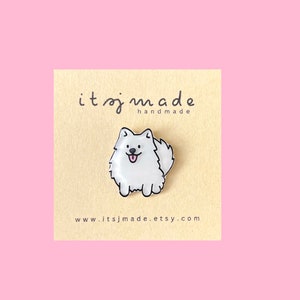 Può includere: Spilla in smalto bianco con un cane di cartone animato con contorni neri. Il cane sorride con la lingua di fuori. La spilla è su una carta bianca con il testo "itsjmade handmade" e "www.itsjmade.etsy.com".