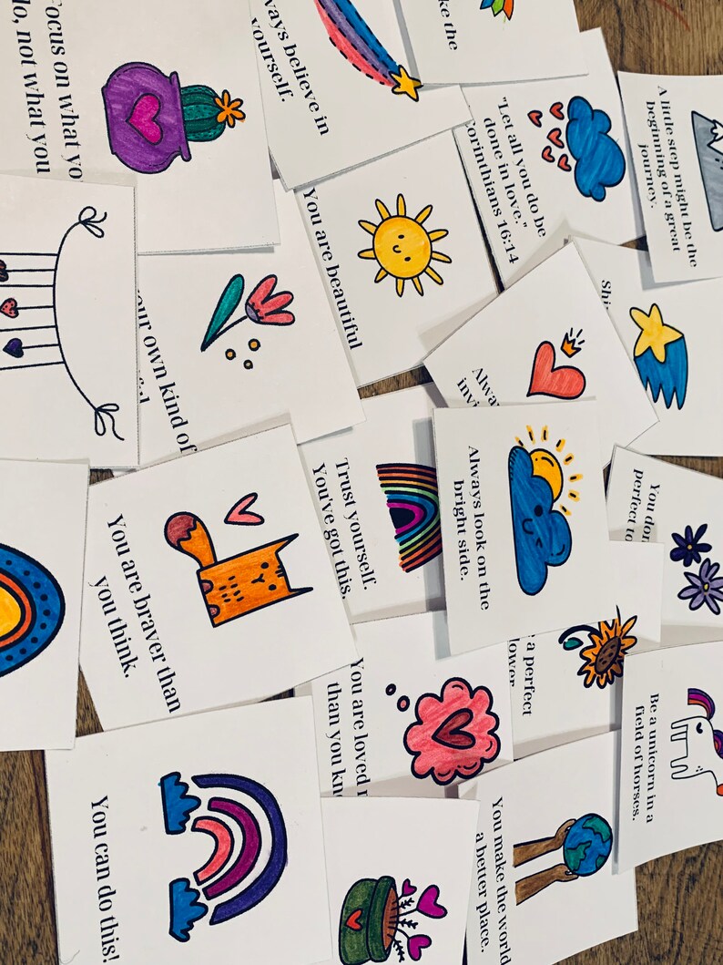May include: A collection of colorful affirmation cards with hand-drawn illustrations and inspirational messages. The cards feature rainbows, hearts, flowers, and other positive imagery. Some of the messages include "You are beautiful", "You are braver than you think", and "Trust yourself. You've got this."