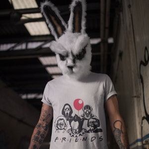May include: A person wearing a white rabbit mask and a grey t-shirt with a graphic of horror movie characters. The shirt says "FRIENDS" and features a red balloon, Ghostface, a character from the movie "The Texas Chainsaw Massacre", and a character from the movie "IT".