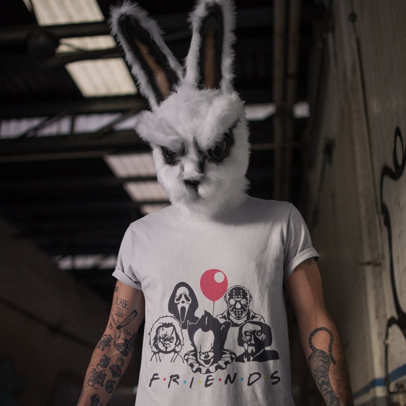May include: A person wearing a white rabbit mask and a grey t-shirt with a graphic of horror movie characters. The shirt says "FRIENDS" and features a red balloon, Ghostface, a character from the movie "The Texas Chainsaw Massacre", and a character from the movie "IT".
