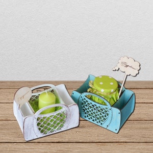 May include: Two wooden gift boxes with decorative cutouts. The box on the left is white with a candle and green grass inside. The box on the right is blue with a green jar with a white lid and white polka dots inside. Both boxes have a small wooden sign with the word "Happy" on it.