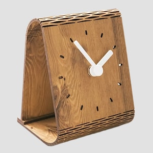 Puede incluir: Un reloj de madera con una esfera y agujas blancas. El reloj está hecho de madera y tiene un diseño único. El reloj está de pie sobre una mesa.