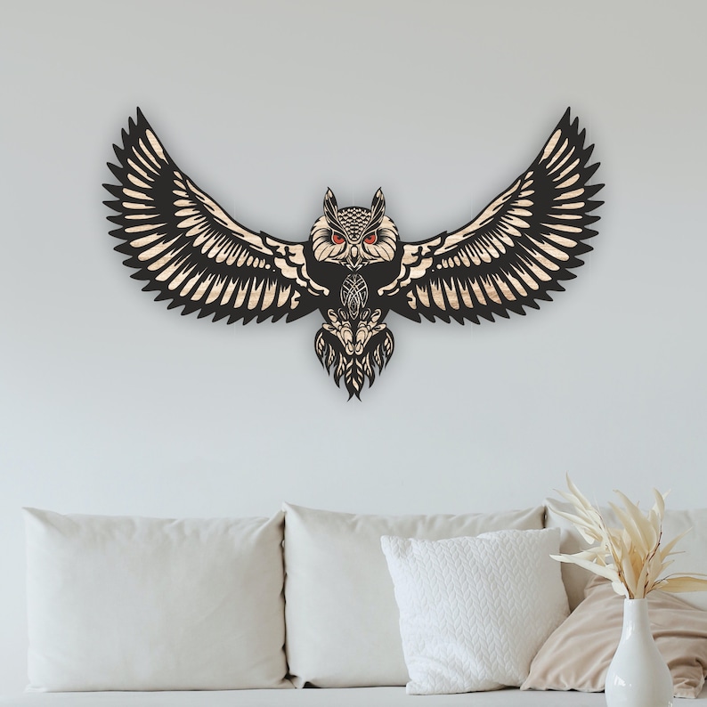 May include: Black wooden owl wall decor with intricate details and red eyes. The owl is in flight with its wings spread wide.