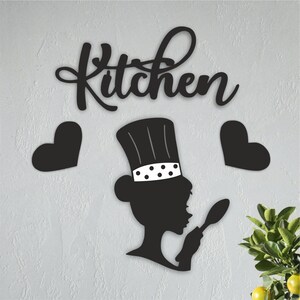 Puede incluir: Decoración de pared de metal negro con la palabra "Cocina" y una silueta de un chef sosteniendo una cuchara. Dos corazones negros están a cada lado del chef.