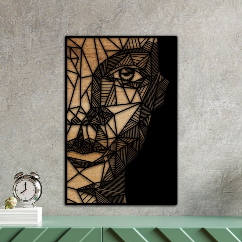 May include: Geometric black and white line art design of a face with one eye visible. The design is on a wood background.