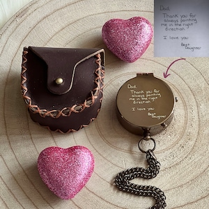 Peut inclure: Une boussole en laiton avec un &eacute;tui en cuir et deux c&oelig;urs en paillettes roses. La boussole porte une inscription qui dit : "Papa, merci de m'avoir toujours guid&eacute; dans la bonne direction. Je t'aime. Ta fille ch&eacute;rie".