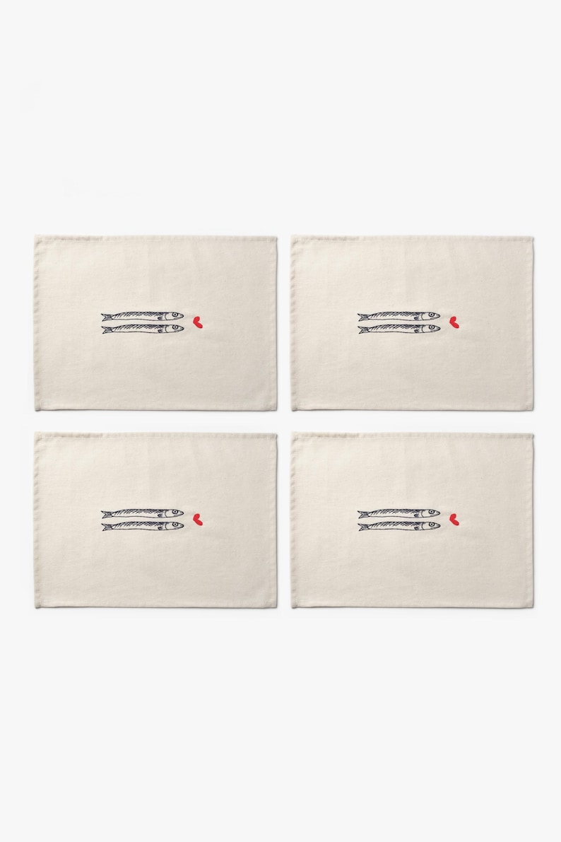 Puede incluir: Cuatro manteles individuales rectangulares de color blanquecino. Cada uno presenta un par de peces azul oscuro estilizados con un peque&ntilde;o coraz&oacute;n rojo. Los peces est&aacute;n dibujados con l&iacute;neas simples, creando un dise&ntilde;o minimalista.