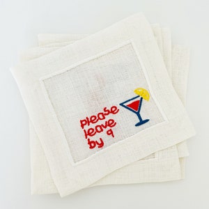 Puede incluir: Juego de cuatro servilletas de c&oacute;ctel de lino blanco con bordado rojo que dice "Please leave by 9" y una copa de c&oacute;ctel roja y azul con una rodaja de lim&oacute;n amarilla.