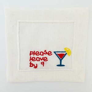 Puede incluir: Servilleta de c&oacute;ctel de lino blanco con bordado rojo que dice "please leave by 9" y una copa de martini roja y azul con una rodaja de lim&oacute;n amarilla.