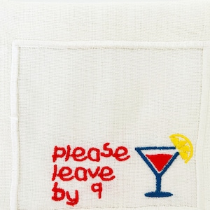Puede incluir: Servilleta de lino blanco con bordado rojo que dice "please leave by 9" y una copa de c&oacute;ctel bordada en azul con una rodaja de lim&oacute;n amarilla.