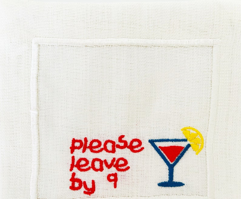 Puede incluir: Servilleta de lino blanco con bordado rojo que dice "please leave by 9" y una copa de c&oacute;ctel bordada en azul con una rodaja de lim&oacute;n amarilla.
