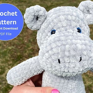 Puede incluir: Un juguete de peluche de hipopótamo gris tejido a crochet con ojos azules. El juguete está siendo sostenido por una mano. La imagen incluye el texto "Crochet Pattern Instant Download PDF File".