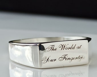 May include: A silver ring with a rectangular band and the inscription "The World at Your Fingertips".