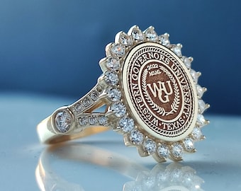 May include: A gold ring with a large oval-shaped stone set in a halo of smaller stones. The stone features the Western Governors University logo and the text "Western Governors University" and "2022 MSML".