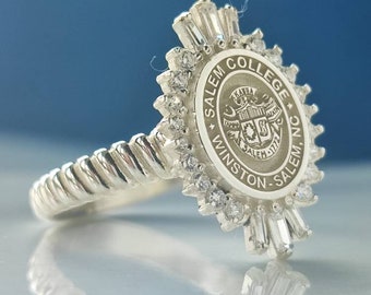 Könnte beinhalten: Ein silberner Ring mit der Aufschrift "Salem College Winston-Salem, NC" um ein zentrales Emblem. Der Ring hat ein gedrehtes Band und ist mit kleinen, klaren Edelsteinen verziert.
