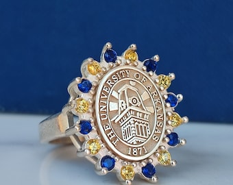 Könnte beinhalten: Ein silberner Ring mit einem Design aus blauen und gelben Steinen. Der Ring zeigt das Logo der University of Arkansas mit den Worten "The University of Arkansas" und "1871".