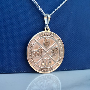 Może przedstawiać: Srebrny naszyjnik z okrągłym wisiorem przedstawiającym cztery symbole: sowę, lwa, wagę i różę. Wisiorek jest ozdobiony napisem "Mądrość", "Odwaga", "Sprawiedliwość" i "Umiarkowanie".