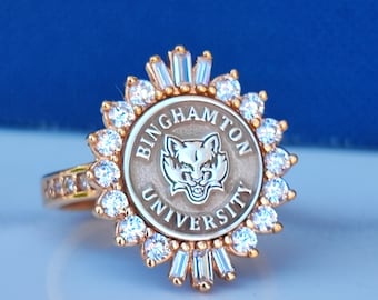 Könnte beinhalten: Ein goldener Ring mit einem runden Design, das das Logo der Binghamton University zeigt, einen Wolfskopf und die Worte "Binghamton University". Der Ring ist mit klaren Zirkonia-Steinen verziert.