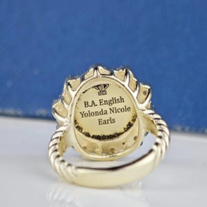 May include: A gold ring with a diamond-shaped design and a band that is twisted. The inside of the ring is engraved with the text "B.A. English Yolanda Nicole Earls 10K".
